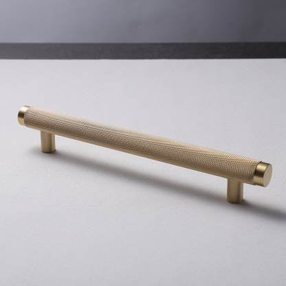 A gold-colored brass handle lying on a flat surface with a plain background.