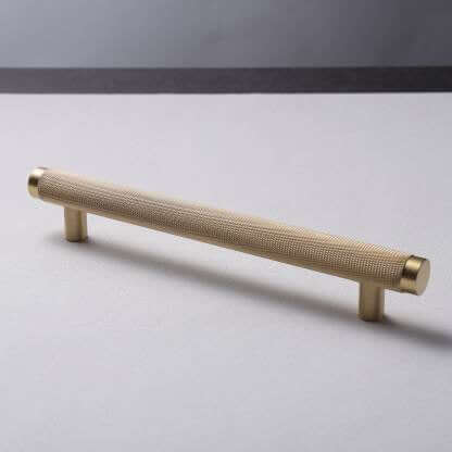A gold-colored brass handle lying on a flat surface with a plain background.