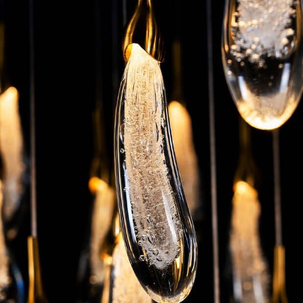 A hand-formed glass pendant light with a silver top, glowing from within, suspended from a cable.