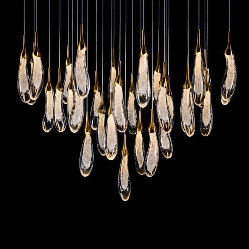 A hand-formed glass pendant light with a silver top, glowing from within, suspended from a cable.