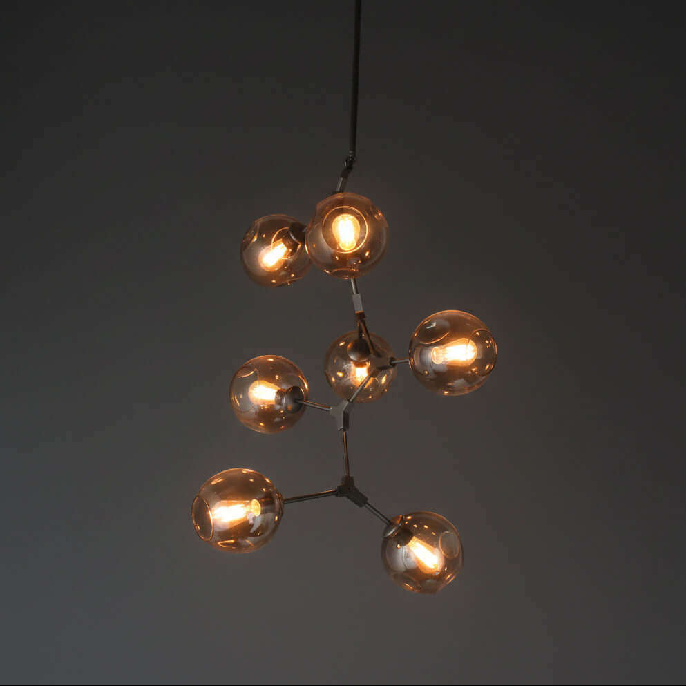A vertical pendant light with multiple glass bulb covers in a warm hue, hanging from adjustable metal arms against a wooden ceiling.