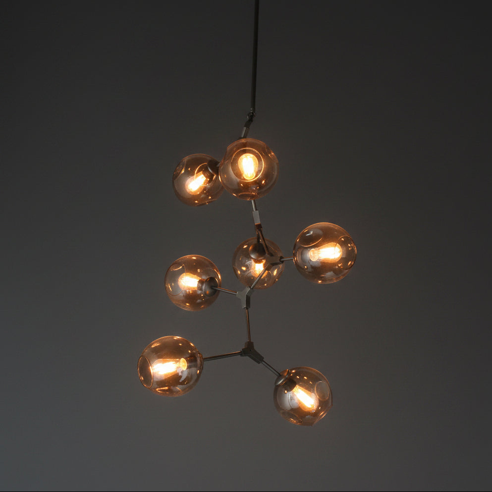 A vertical pendant light with multiple glass bulb covers in a warm hue, hanging from adjustable metal arms against a wooden ceiling.