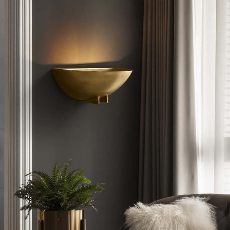 A minimalist half round wall sconce with a warm light, finished in either brushed brass or blackened iron, mounted on a wall.