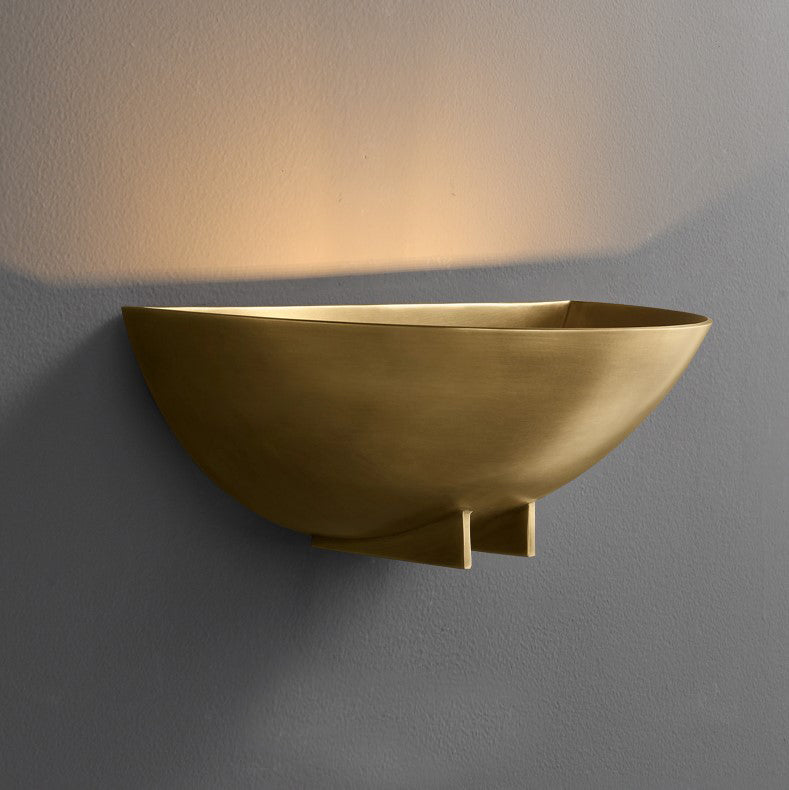 A minimalist half round wall sconce with a warm light, finished in either brushed brass or blackened iron, mounted on a wall.