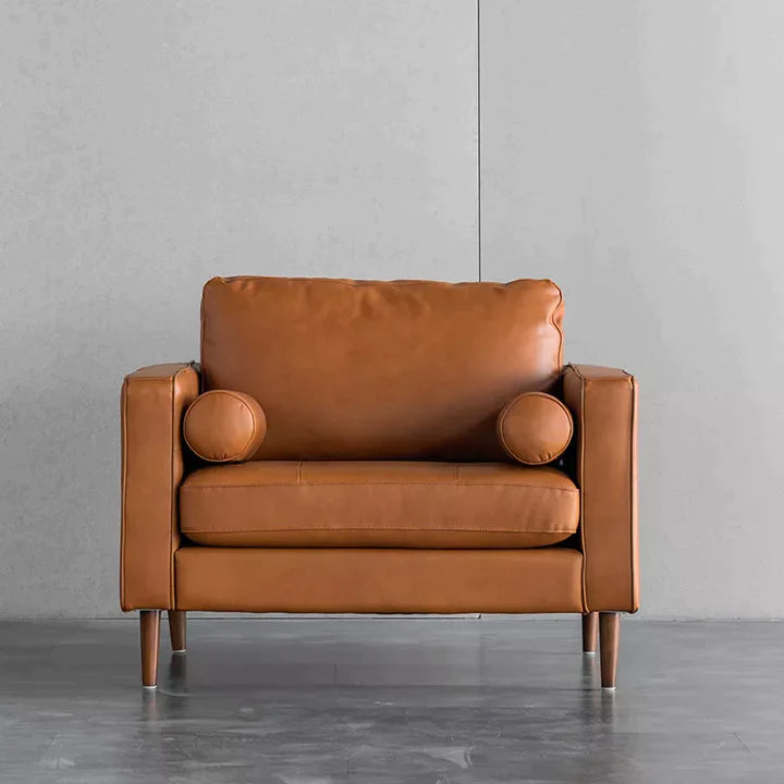 A brown genuine leather sofa with a wooden frame and legs, displayed in a room with a simple gray backdrop.
