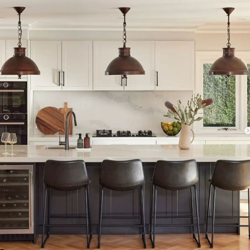 Vintage style brass pendant lights with a matte white interior hanging over a kitchen island with bar stools.