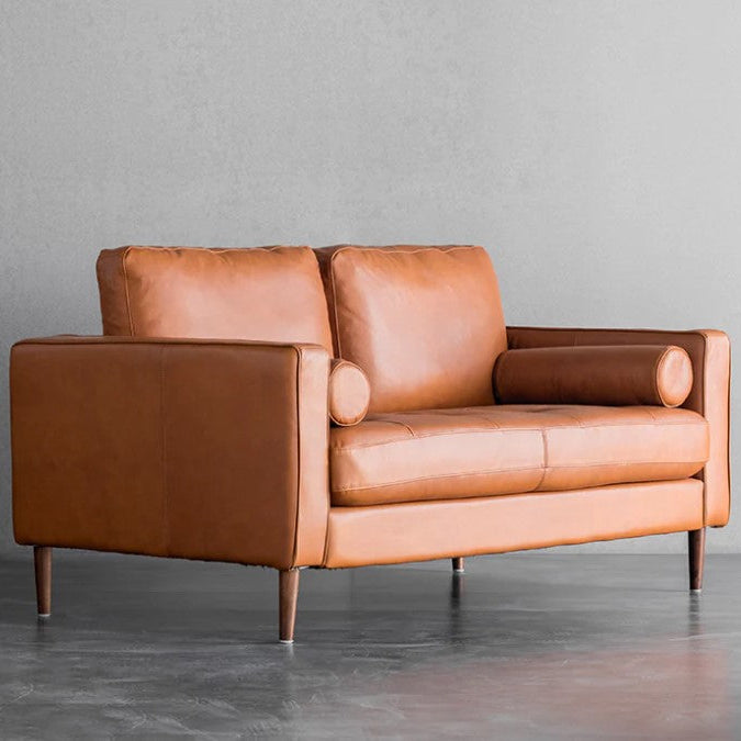 A brown genuine leather sofa with a wooden frame and legs, displayed in a room with a simple gray backdrop.
