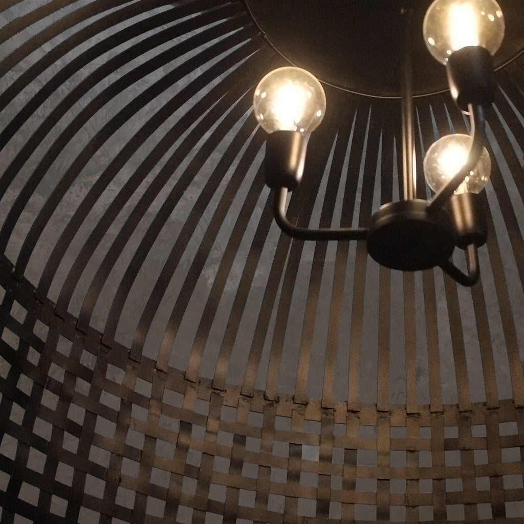 Close-up of a chandelier with three lit bulbs against a woven basket background
