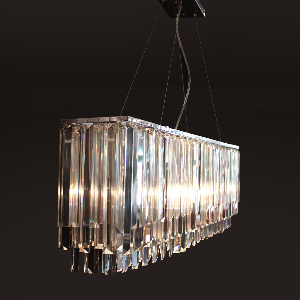 A modern rectangular chandelier with clear prismatic crystals, suspended by thin cables against a dark background.