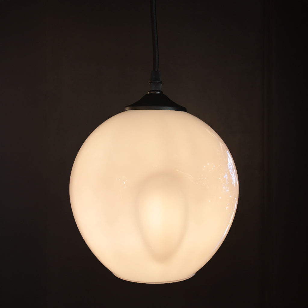 A spherical frosted glass pendant light glowing with a warm cream-white light, suspended by a black cord against a very dark, near-black background.