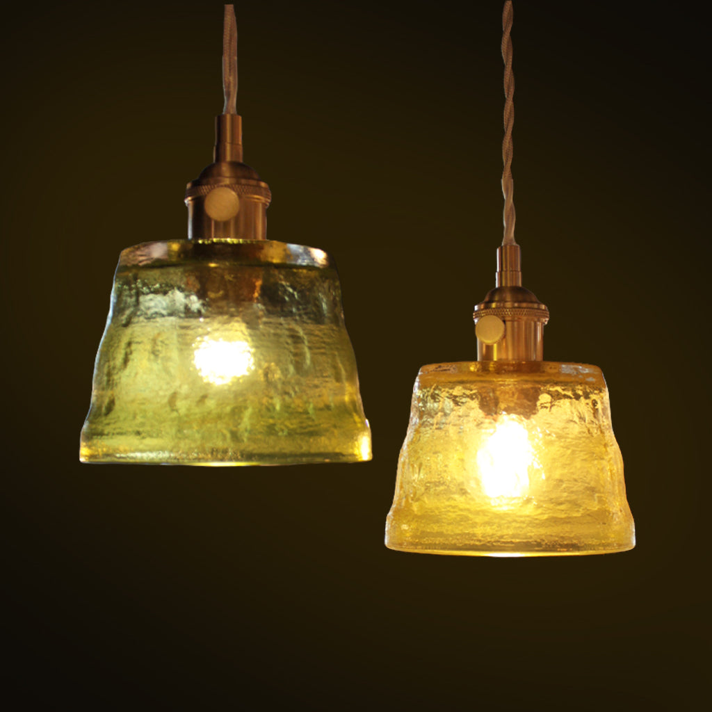 Two hanging pendant lights with textured green glass shades and warm brass-toned metal fixtures, shown against a dark background.
