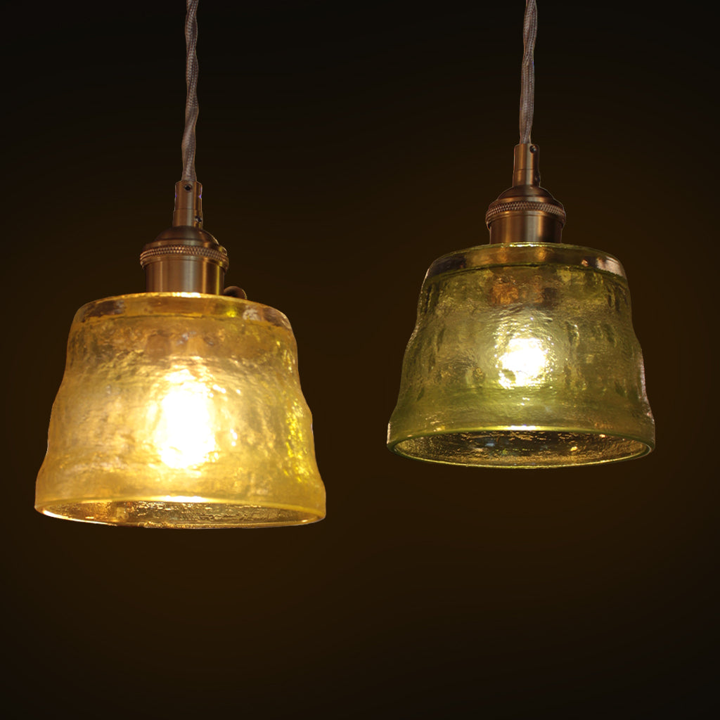 Two hanging pendant lights with textured glass shades, one glowing green-yellow and the other green, suspended against a dark background.