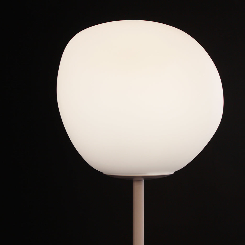 A modern floor lamp featuring a large, organic-shaped frosted white glass globe shade on a slim white metal stand, set against a solid black background.