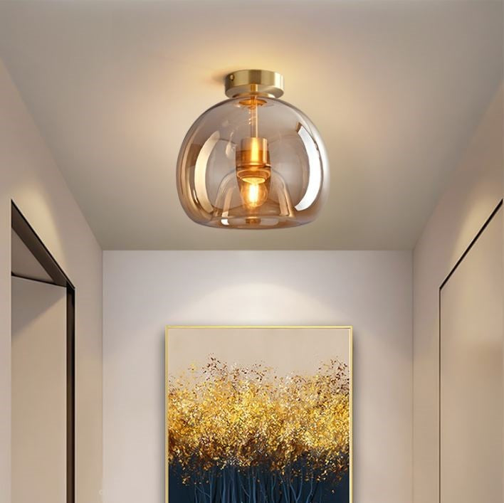 A Deon ceiling light with a tinted amber glass shade and brass fittings, installed in a room above a wall painting.