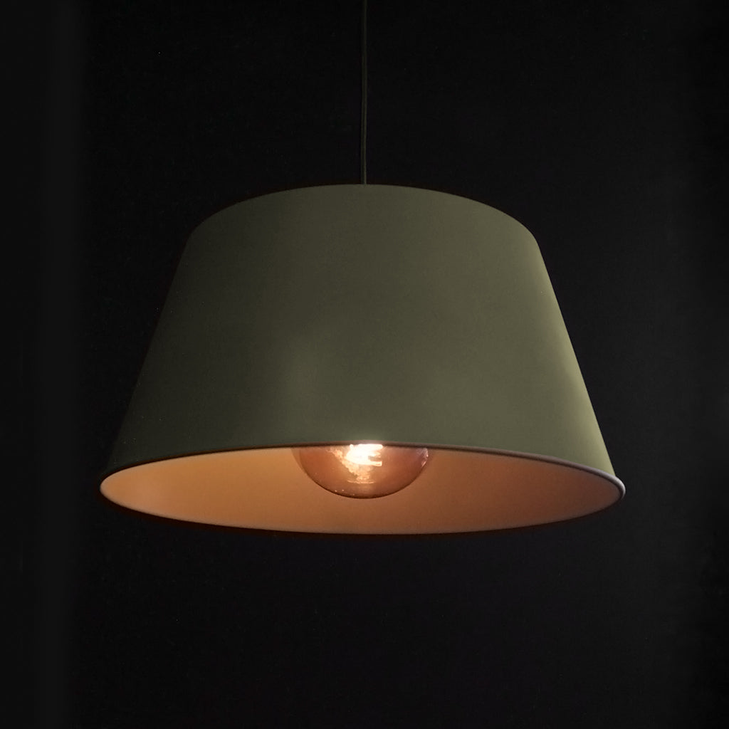 Green pendant lamp with a lit bulb against a black background