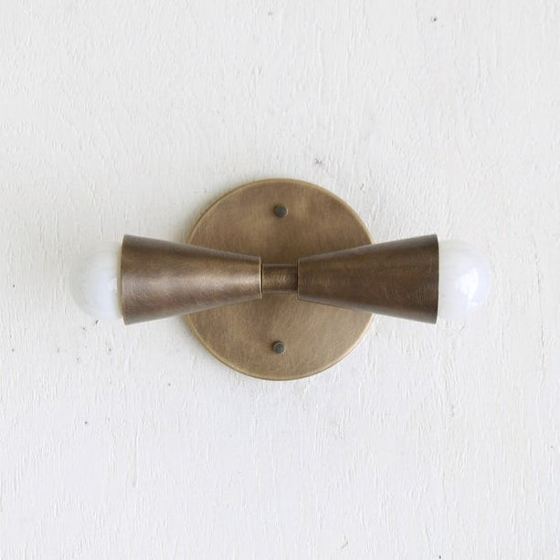 Brass wall sconce with two cylindrical shades on a white background
