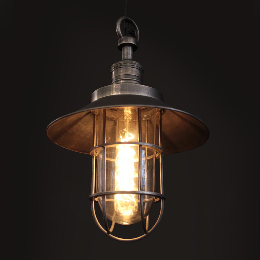 Industrial-style pendant light with a wide metal canopy, wire cage guard, and glowing warm bulb inside a dark background.
