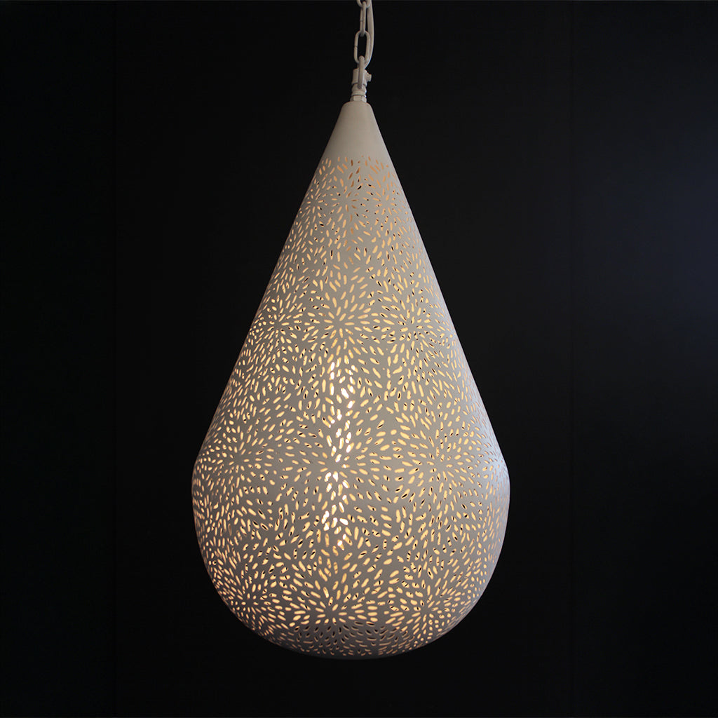 A teardrop-shaped hanging pendant light with a white perforated metal shade casting a warm yellow glow against a solid black background.