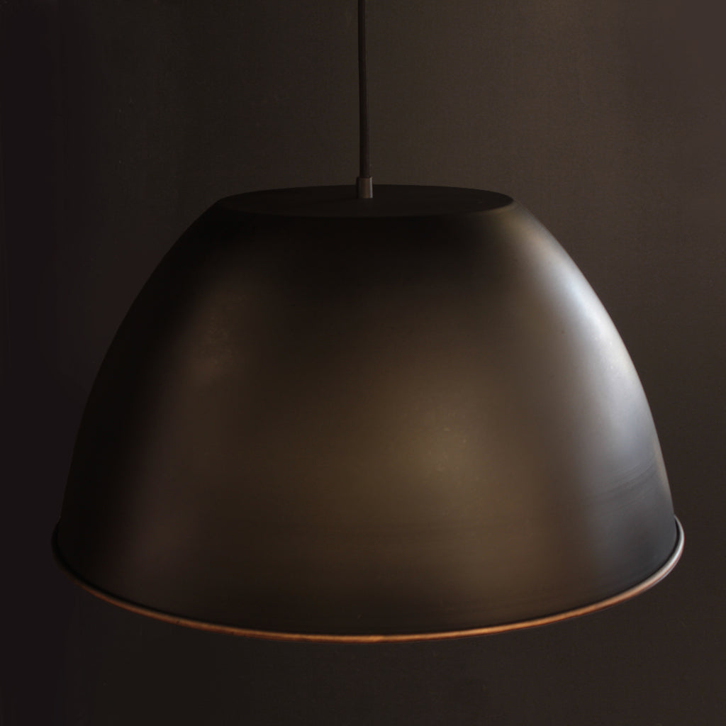 Metal domed pendant shade with black exterior and textured bronze interior against a dark background