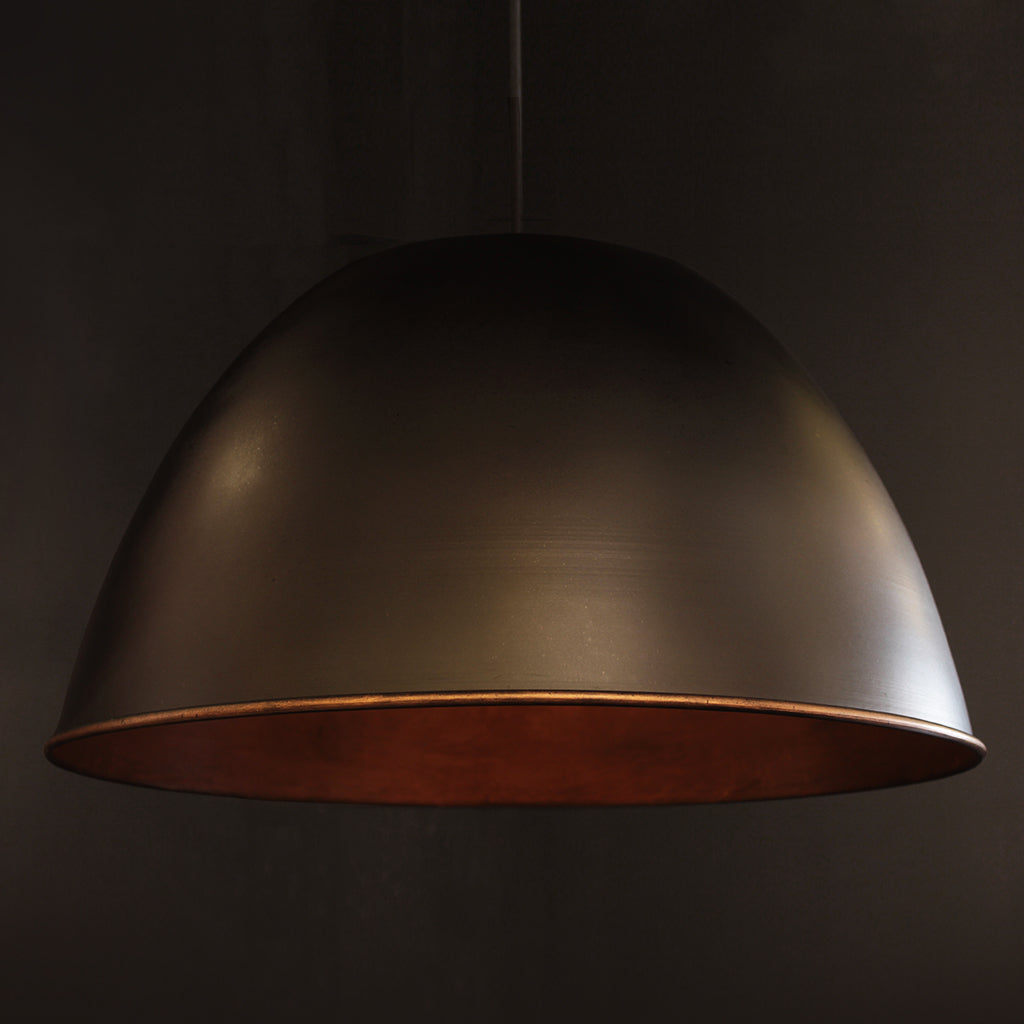 Metal domed pendant shade with black exterior and textured bronze interior against a dark background