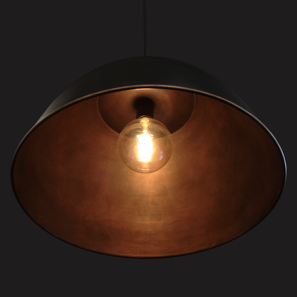 Metal domed pendant shade with black exterior and textured bronze interior against a dark background