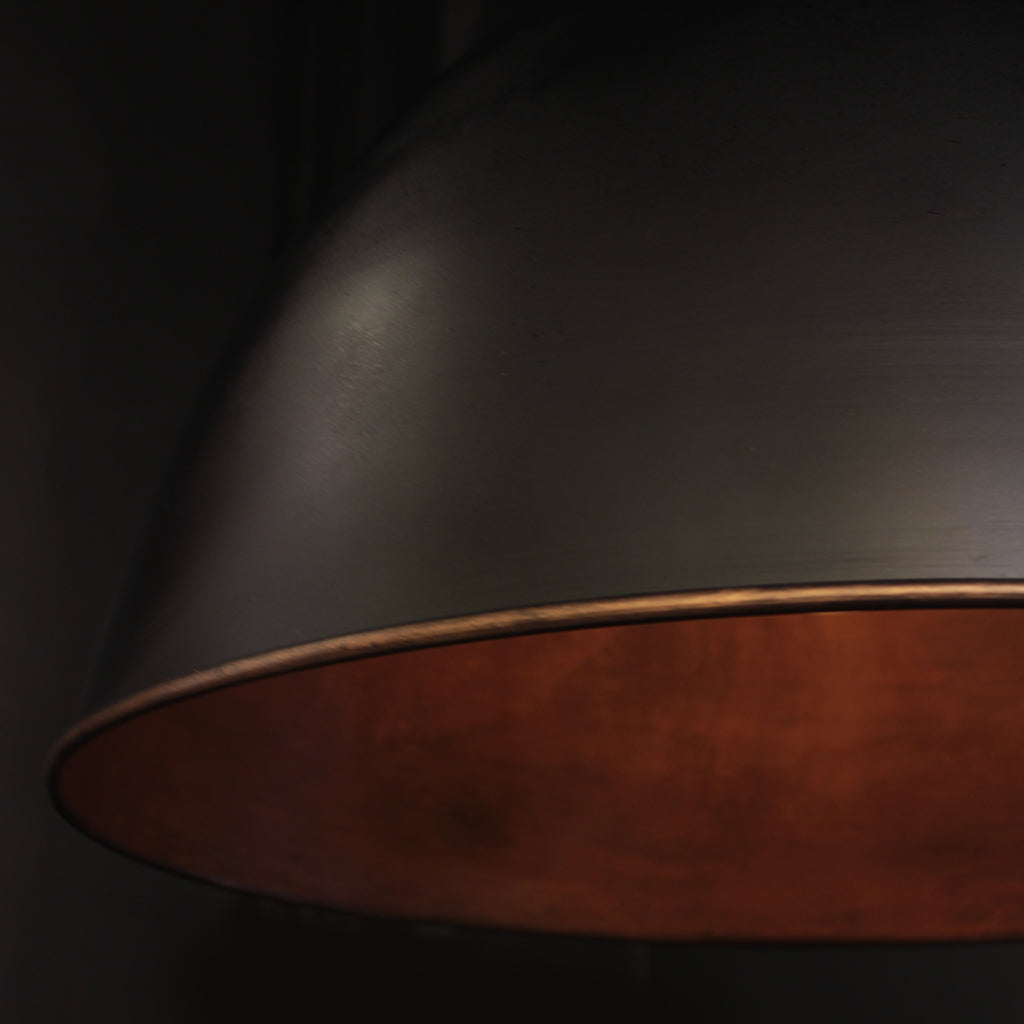 Metal domed pendant shade with black exterior and textured bronze interior against a dark background