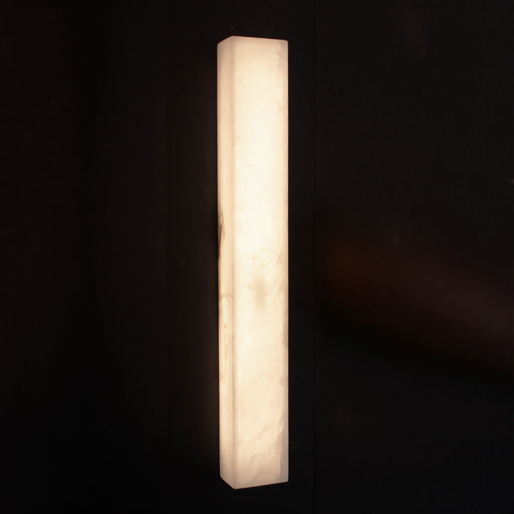 A modern rectangular wall sconce made of glowing white stone, casting a warm light against a dark background.