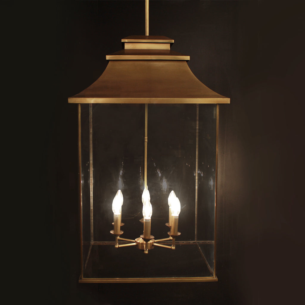 Brass lantern style pendant light with tiered top and glass panels against dark background
