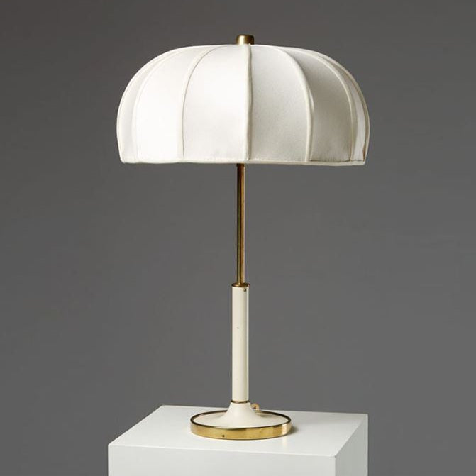 Table lamp with white shade, black base, and gold accents on a gray background