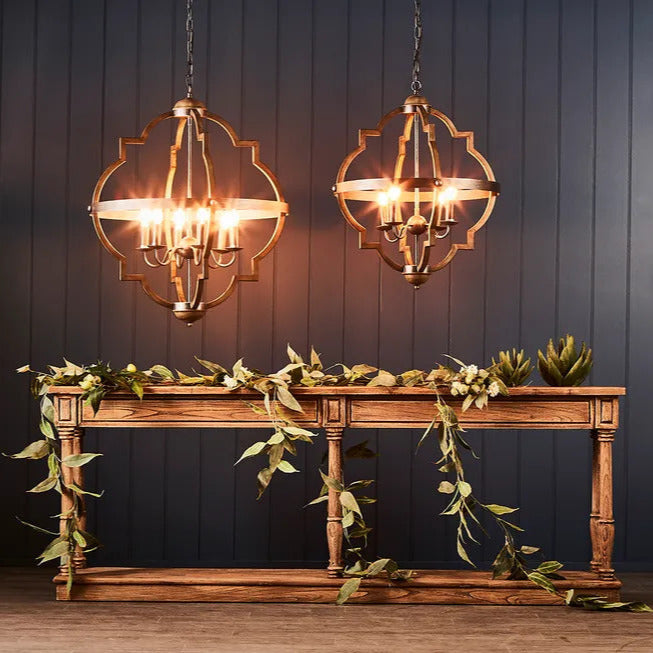 Two brass chandeliers with a geometric structure, hanging against a dark background. One chandelier is illuminated, showcasing its intricate design and multiple light bulbs.