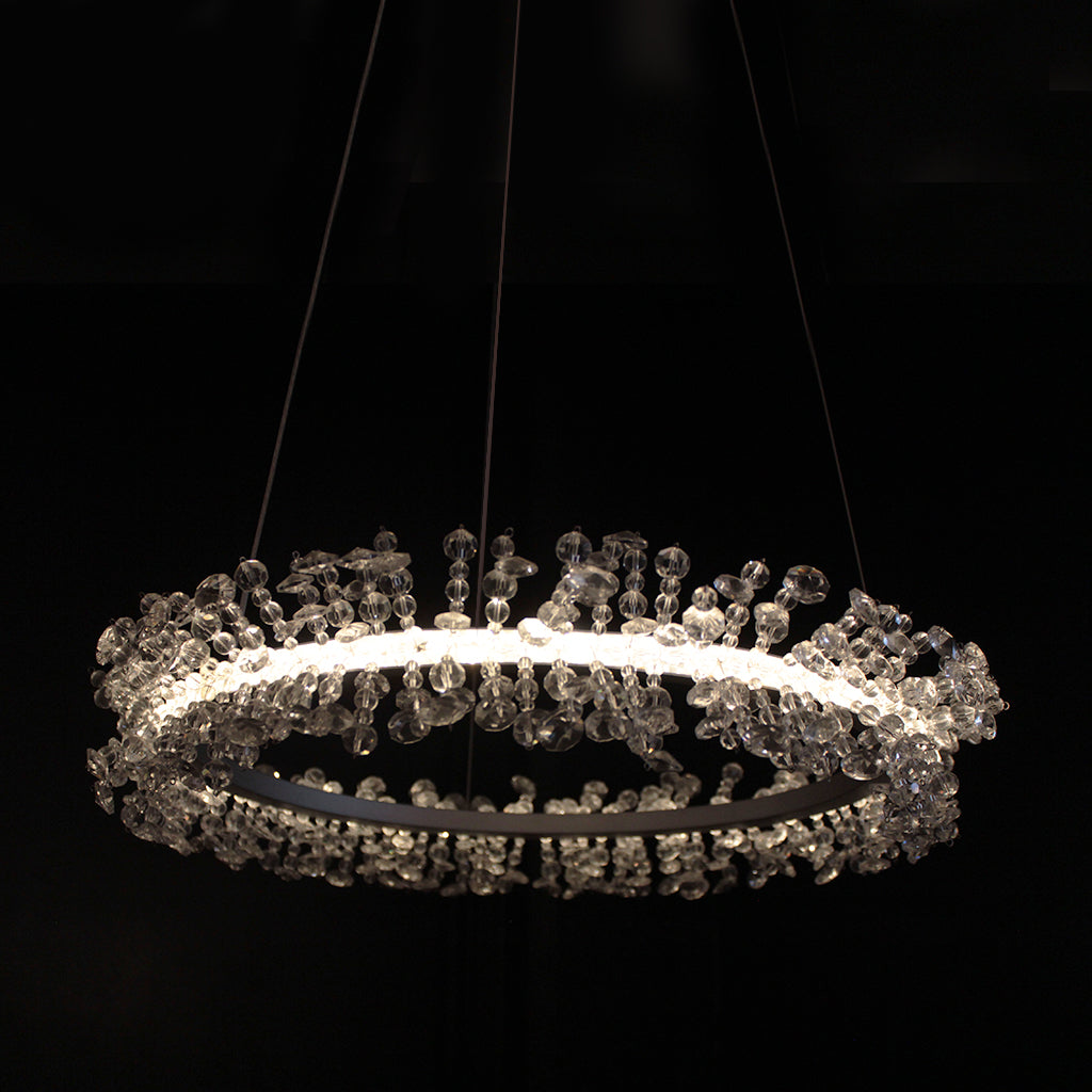 A modern circular LED chandelier with clear crystal beads, suspended against a solid black background.