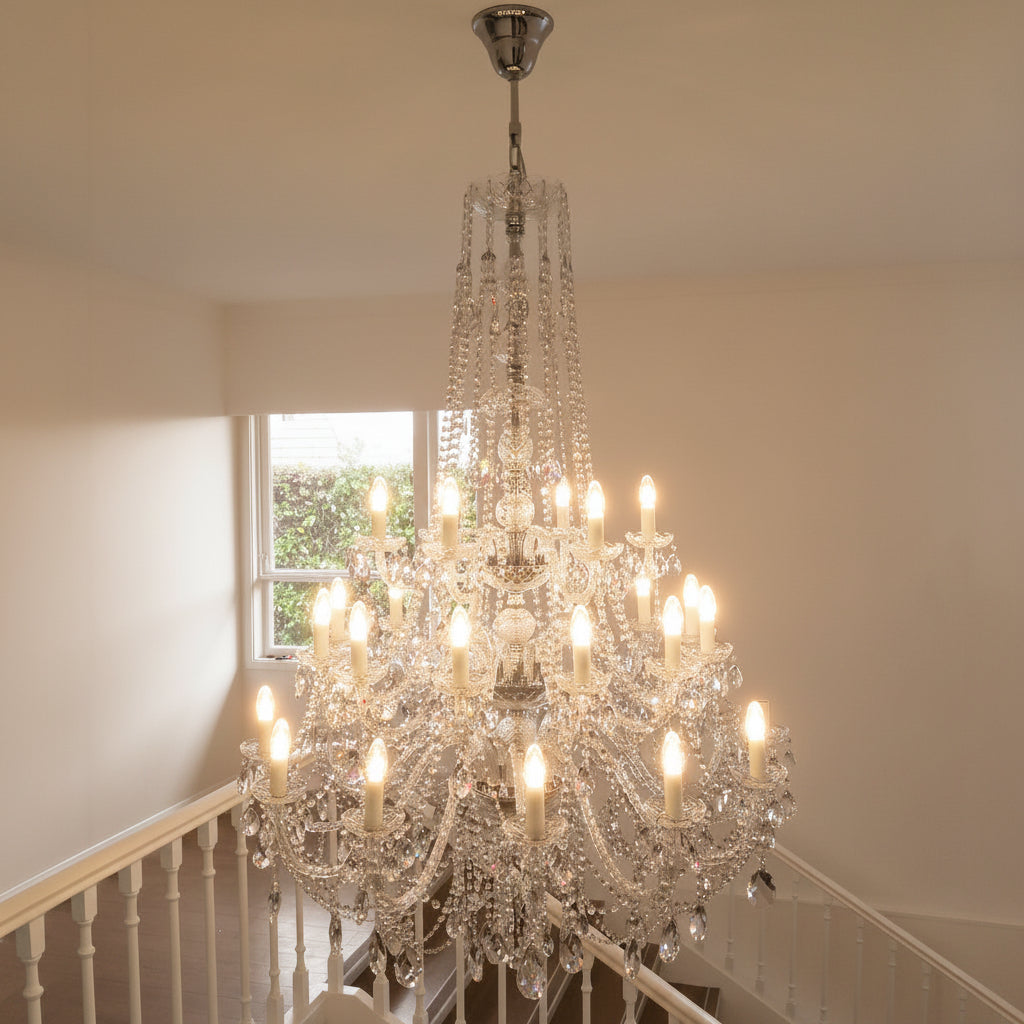 Crystal chandelier hanging in a room with a window and staircase.