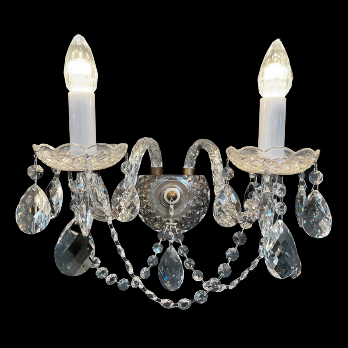 A wall light fixture with clear, highly-faceted crystal decorations and antique brass accents.