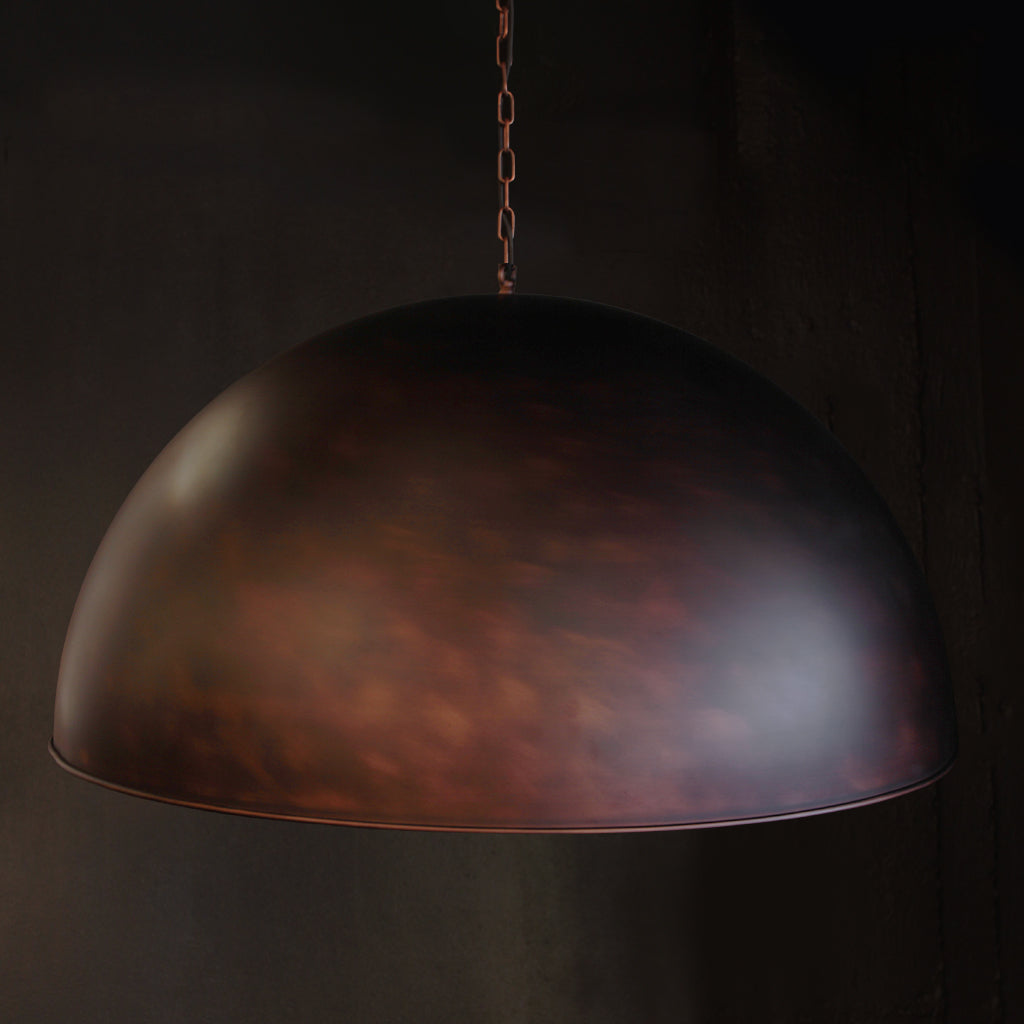 A dome-shaped pendant light with a textured metallic finish in dark bronze and copper tones, suspended by a chain against a dark background.
