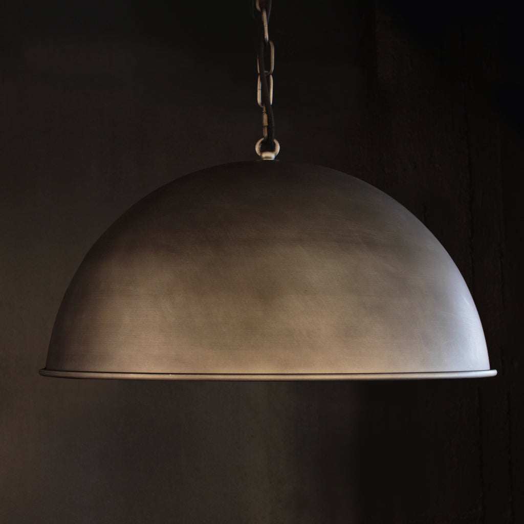 A dome-shaped pendant light with a dark, textured metallic finish hanging from a chain against a dark background.
