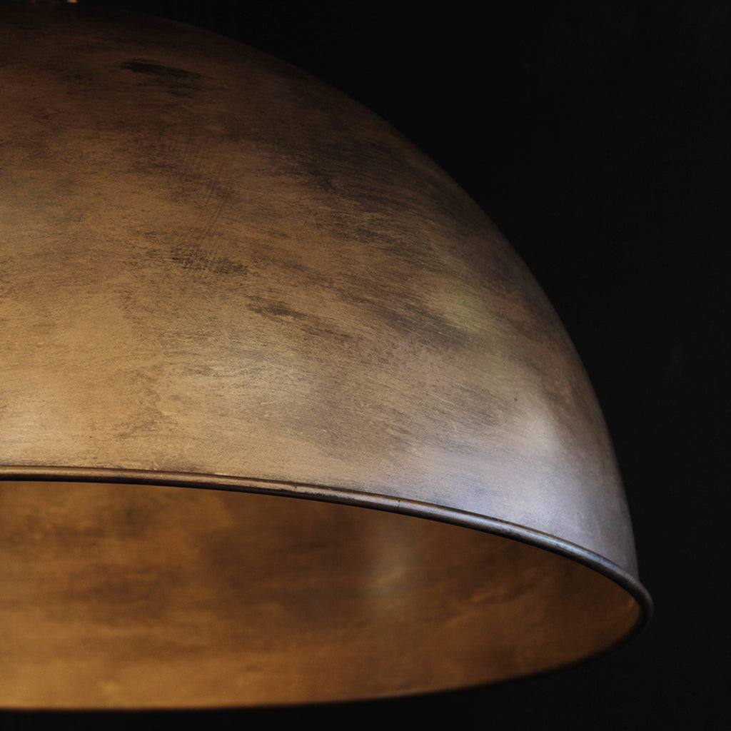 Close-up of a dome-shaped metal lamp shade in a warm brass finish, showing the textured outer surface and the darker interior, set against a black background.