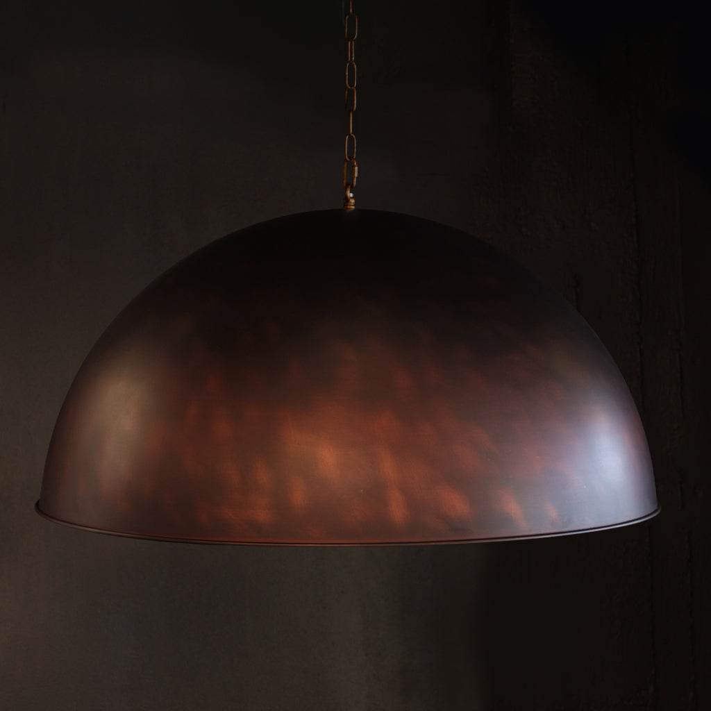 A large dome-shaped pendant light with a hammered metallic finish in a dark bronze or copper tone, suspended by a chain against a dark background.