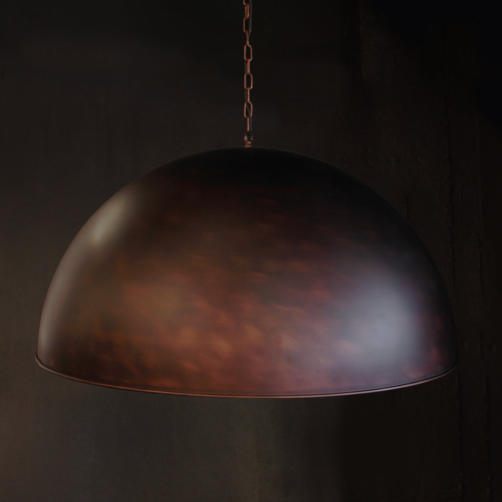 A dome-shaped pendant light with a textured metallic finish in dark bronze and copper tones, suspended by a chain against a dark background.
