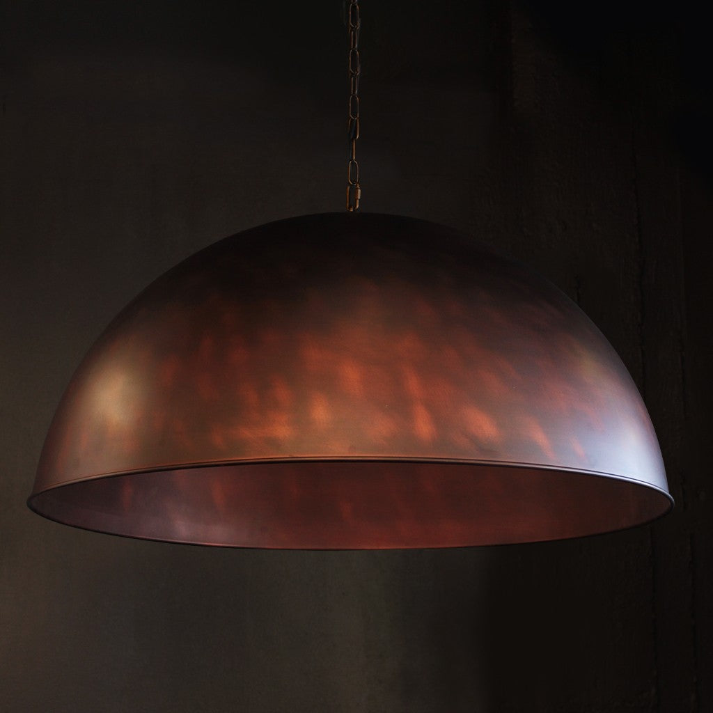 A large dome-shaped pendant light with a metallic finish in warm copper and bronze tones, suspended by a chain against a dark background.