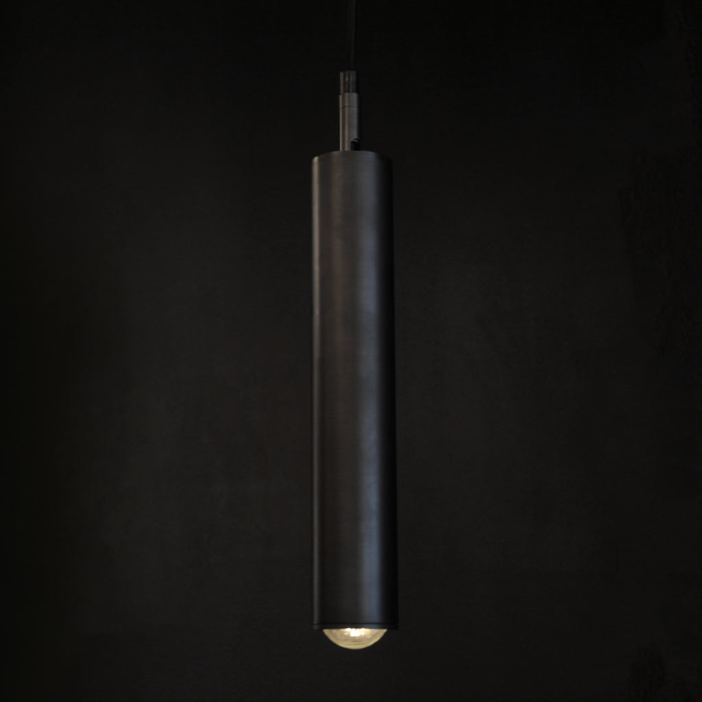 A modern gunmetal dark cylindrical pendant light hanging in front of a dark background