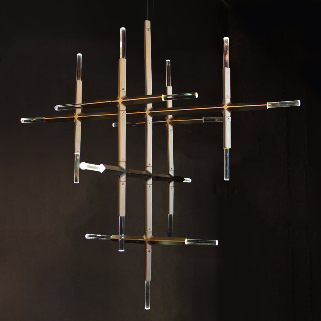 A modern multi-arm chandelier with clear crystal cylindrical tubes and warm brass-finished rods, suspended against a dark background.
