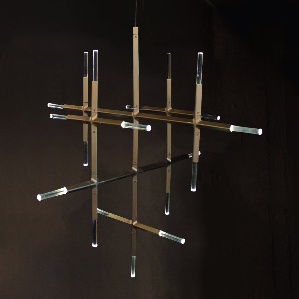 A modern chandelier with a gold-toned geometric metal frame and clear crystal cylindrical tubes, suspended against a dark background.