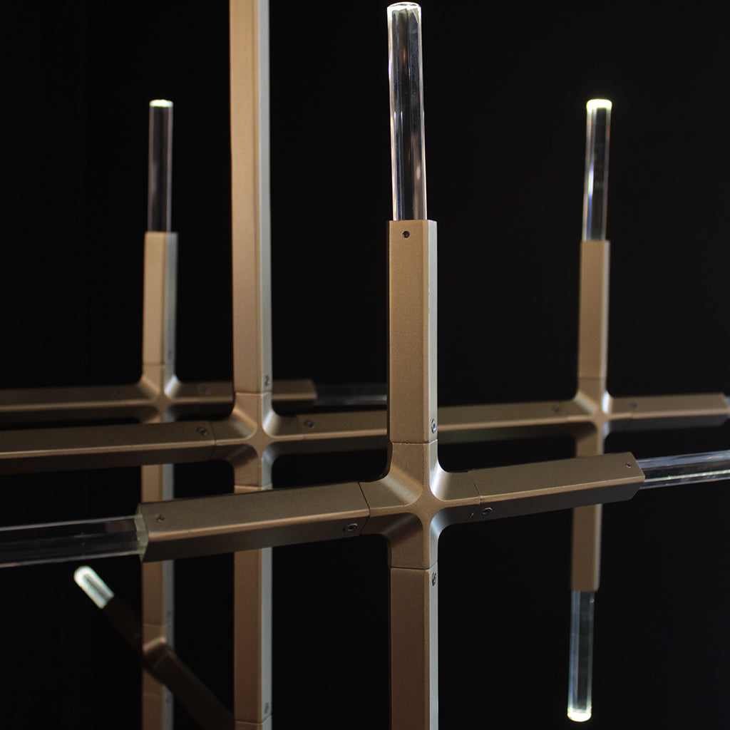 A modern chandelier with a brushed gold metal frame and clear crystal cylindrical shades, shown against a solid black background.