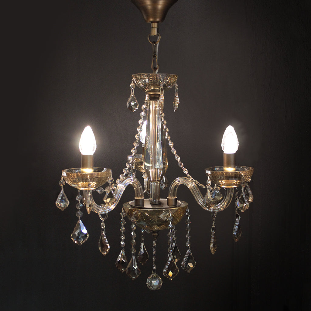 Crystal chandelier with three lit bulbs against a dark background