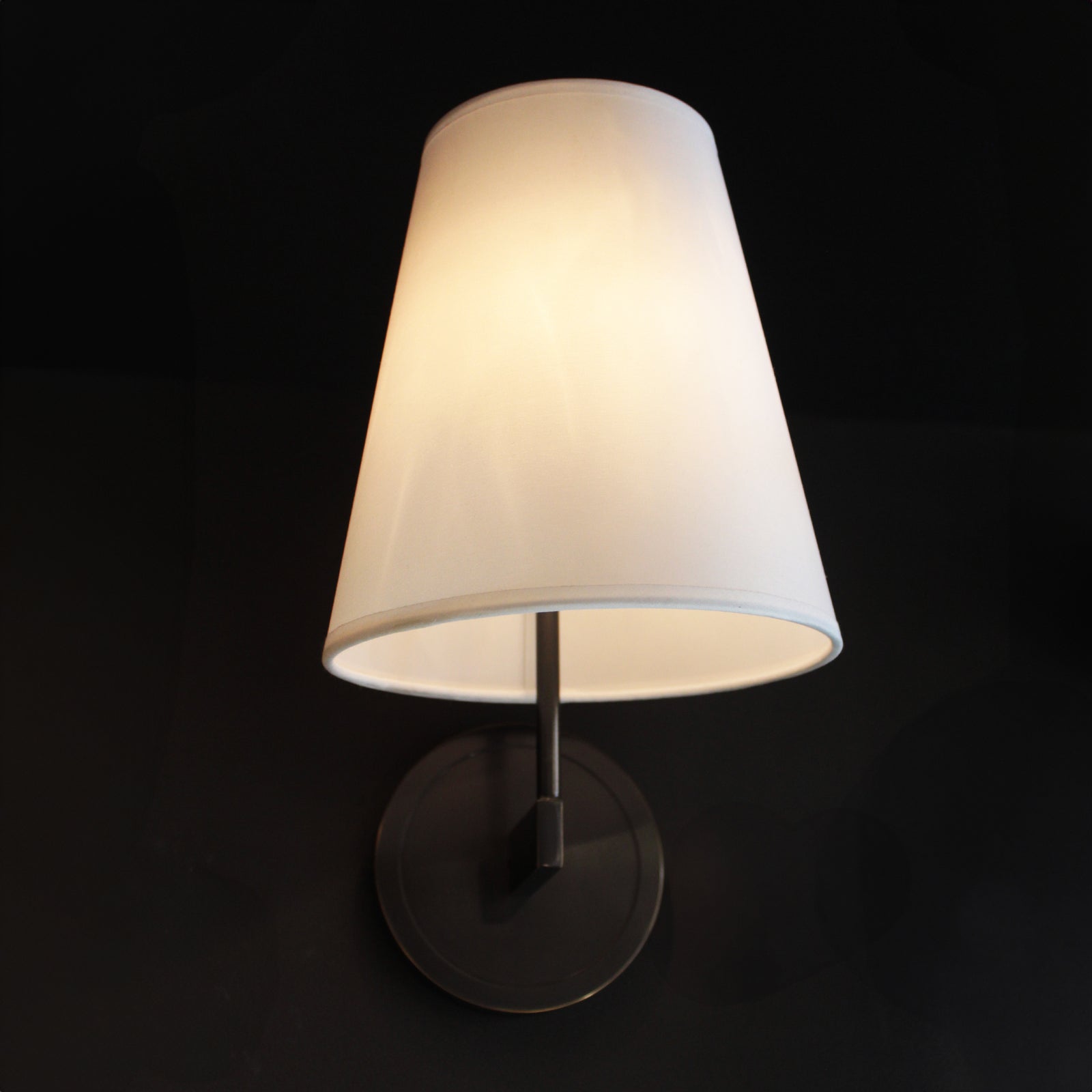 Wall-mounted lamp with a white shade on a black background
