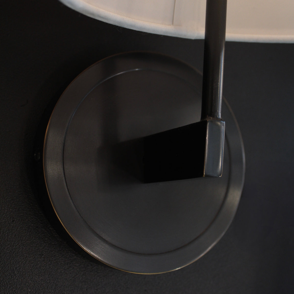 Close-up of a wall-mounted lamp with a dark base and beige shade on a black background