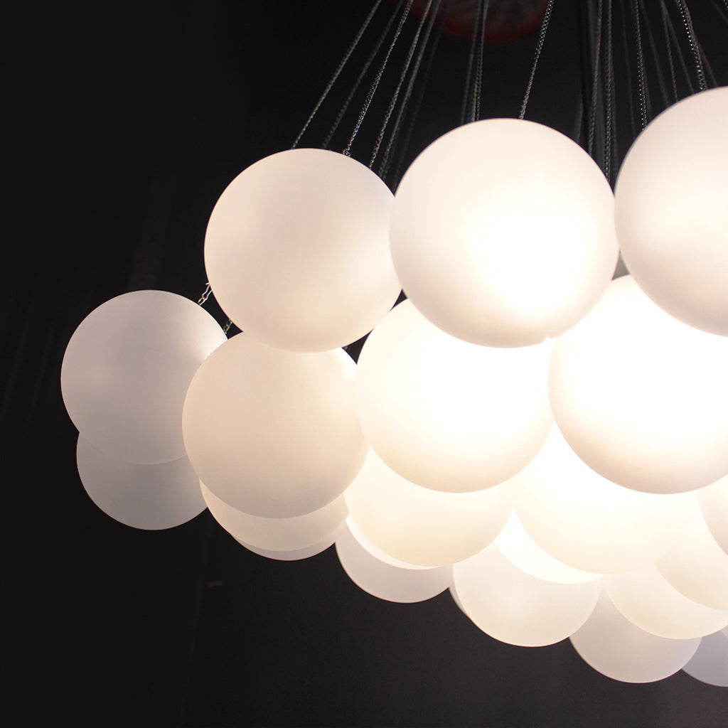 A cluster of frosted white spherical pendant lights suspended by thin chains against a dark background.
