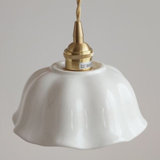 A white ceramic pendant light with a rippled design and brushed brass fittings, hanging against a soft-lit background.