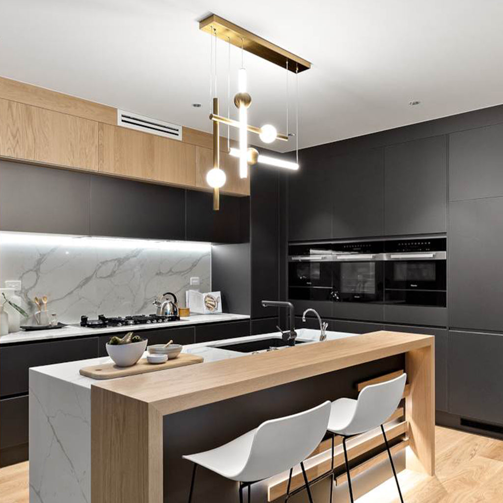 Modern kitchen interior with a central island, two white bar stools, black cabinetry, wood upper cabinets, marble backsplash, and a multi-light pendant chandelier.