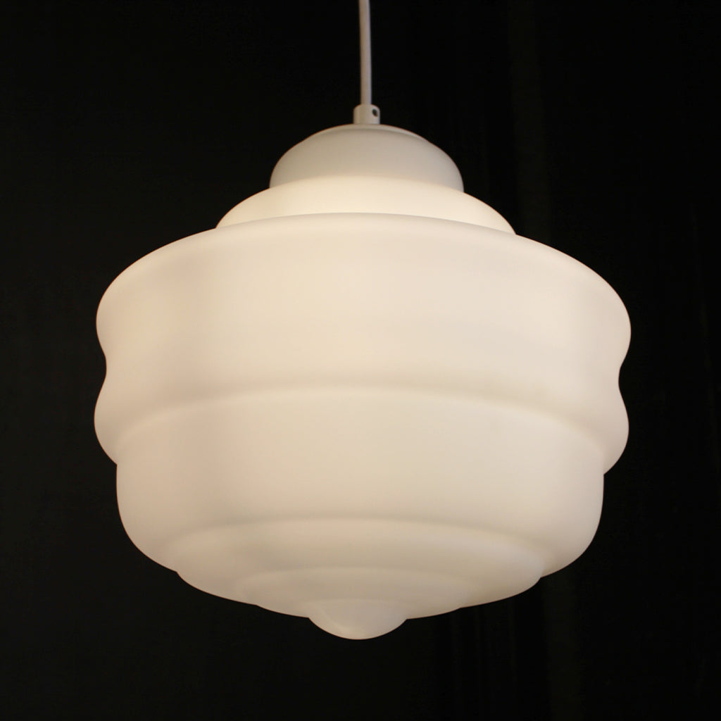 A modern, tiered pendant light with a glowing white frosted glass shade, suspended by a thin cord against a dark, textured background.